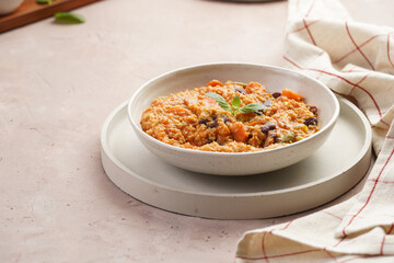Grain dish - Millet with tomatoes, beans, carrots and spices, mint in a white bowl on a concrete round tray with checkered linen kitchen towel on purple background