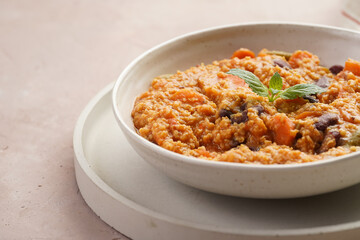 Grain dish - Millet with tomatoes, beans, carrots and spices, mint in a white bowl on a concrete round tray with checkered linen kitchen towel on purple background