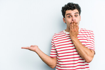 Young caucasian man isolated on blue background impressed holding copy space on palm.