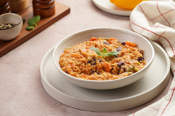 Grain dish - Millet with tomatoes, beans, carrots and spices, mint in a white bowl on a concrete round tray with checkered linen kitchen towel on purple background