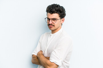 Young caucasian man isolated on blue background frowning face in displeasure, keeps arms folded.