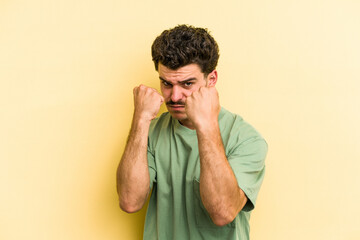 Young caucasian man isolated on yellow background showing fist to camera, aggressive facial...