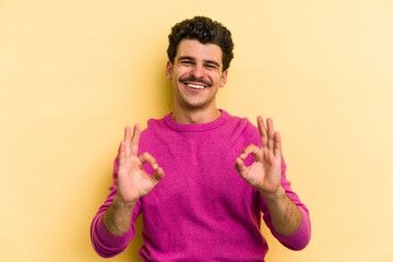 Young caucasian man isolated on yellow background cheerful and confident showing ok gesture.