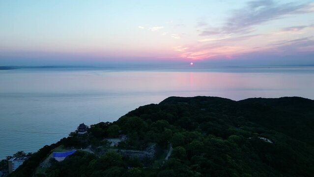 Slow aerial pullback on Sumuto Castle on overlooking ocean at sunrise