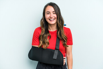 Young caucasian woman with broke hand isolated on blue background laughing and having fun.