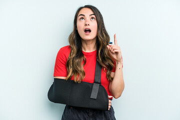 Young caucasian woman with broke hand isolated on blue background pointing upside with opened mouth.