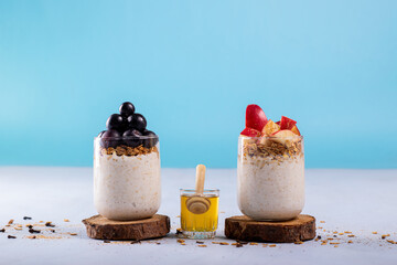 Two overnight oats with black grapes fruits and apple fruits, accompanied with honey. Photo with a blue background and space to add text. Cinnamon, oatmeal, and cloves are scattered on the surface.