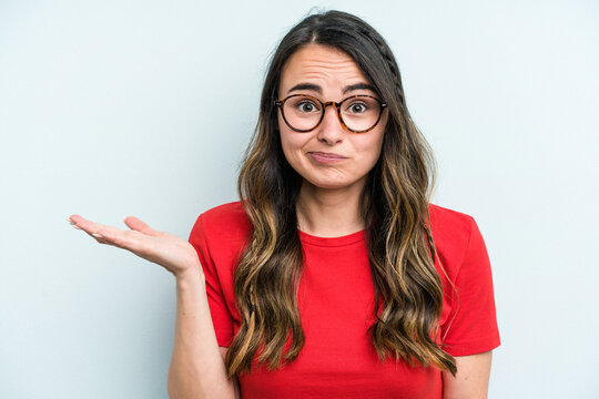 Young caucasian woman isolated on blue background doubting and shrugging shoulders in questioning gesture.