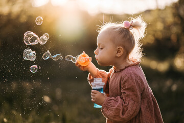 Portrait of funny lovely little girl blowing soap bubbles