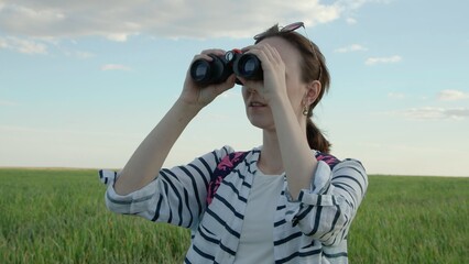 4K. A woman looks through binoculars. Standing in an endless green field