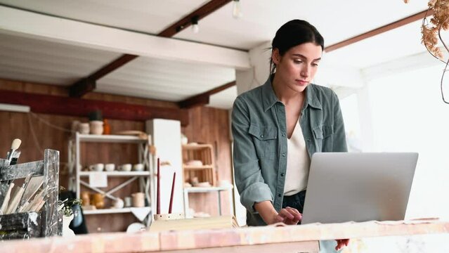 Serious brunette woman working on laptop in the workshop
