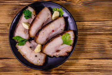 Slices of baked pork belly, garlic and parsley on a black plate. Top view