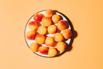 top view of apricots in round plate on orange background