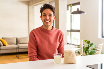 Fototapeta na wymiar Young mixed race man eating oatmeal and milk for breakfast in his kitchen happy, smiling and cheerful.