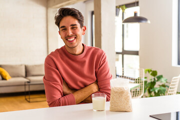 Young mixed race man eating oatmeal and milk for breakfast in his kitchen laughing and having fun.