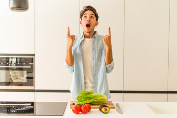 Young mixed race man preparing a salad for lunch pointing upside with opened mouth.