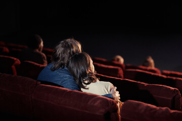 Rear view of affectionate couple embracing while watching movie on comfortable seats in cinema - obrazy, fototapety, plakaty