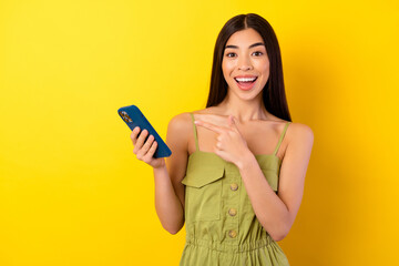 Photo of cute excited lady wear green outfit pointing modern device isolated yellow color background