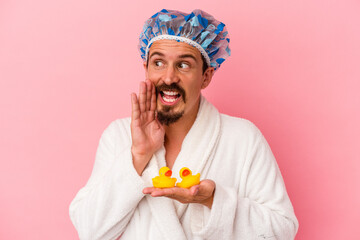 Young caucasian man going to the shower with rubber ducks isolated on pink background shouting and holding palm near opened mouth.
