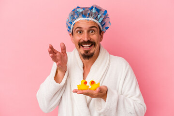 Young caucasian man going to the shower with rubber ducks isolated on pink background receiving a...