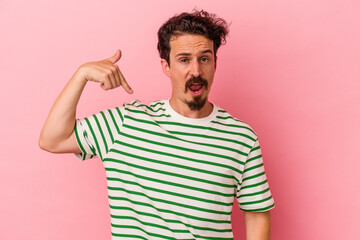 Young caucasian man isolated on pink background person pointing by hand to a shirt copy space, proud and confident