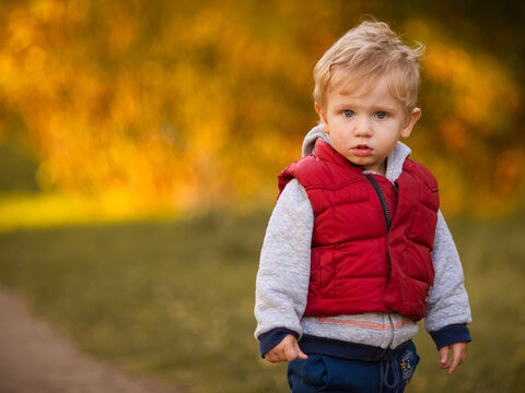 Blond Boy In A Red Vest On An Autumn Walk