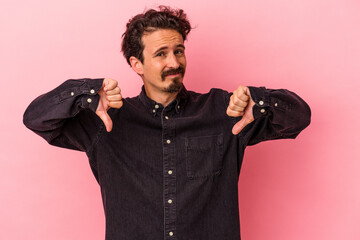 Young caucasian man isolated on pink background showing thumb down, disappointment concept.