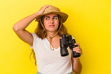 Young caucasian woman holding binoculars isolated on yellow background  being shocked, she has...