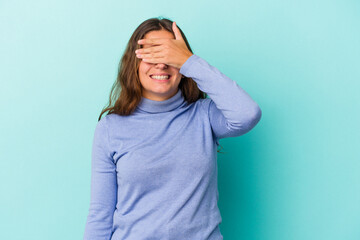 Young caucasian woman isolated on blue background  covers eyes with hands, smiles broadly waiting...
