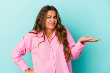 Young caucasian woman isolated on blue background  doubting and shrugging shoulders in questioning...