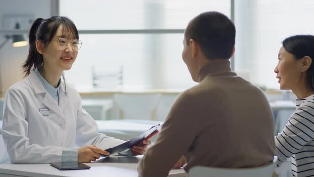 Asian female doctor giving consultation to family couple while working in maternity clinic