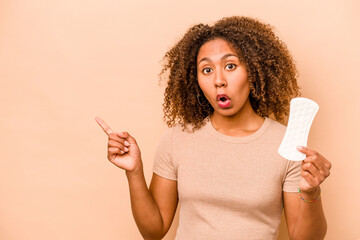Young African American woman holding sanitary napkin isolated on beige background pointing to the...