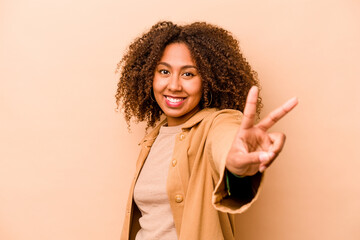 Young African American woman isolated on beige background joyful and carefree showing a peace symbol with fingers.