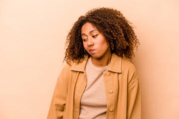 Young African American woman isolated on beige background shrugs shoulders and open eyes confused.