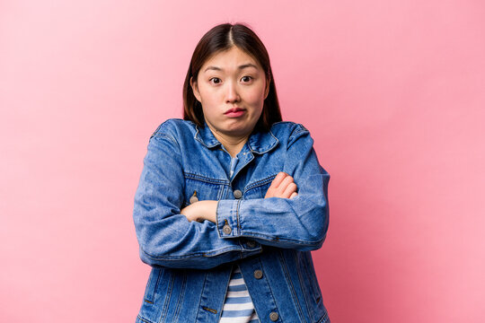 Young Chinese woman isolated on pink background shrugs shoulders and open eyes confused.