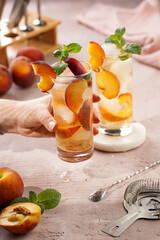 Two glasses with refreshing summer cocktail with ice cubes, peach slices and fresh mint on pale purple background