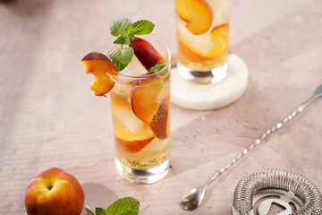 Two glasses with refreshing summer cocktail with ice cubes, peach slices and fresh mint on pale purple background