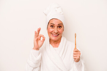 Middle age caucasian woman wearing a bathrobe holding toothbrush isolated on white background cheerful and confident showing ok gesture.