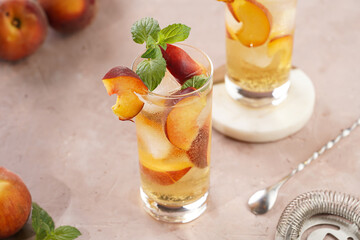 Two glasses with refreshing summer cocktail with ice cubes, peach slices and fresh mint on pale...