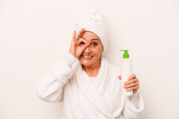 Middle age caucasian woman wearing a bathrobe holding body cream isolated on white background excited keeping ok gesture on eye.