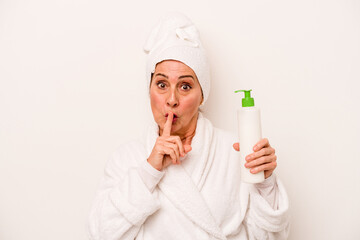 Middle age caucasian woman wearing a bathrobe holding body cream isolated on white background keeping a secret or asking for silence.