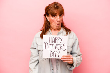 Middle age caucasian woman holding Happy mother’s day placard isolated on pink background shrugs...