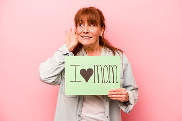 Fototapeta na wymiar Middle age caucasian woman holding I love mom placard isolated on pink background trying to listening a gossip.
