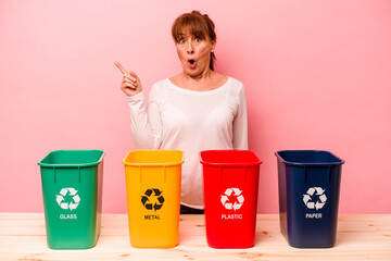 Middle age woman recycling isolated on pink background pointing to the side