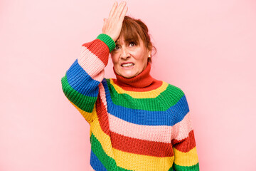 Middle age caucasian woman isolated on pink background forgetting something, slapping forehead with...