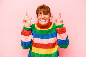 Middle age caucasian woman isolated on pink background crossing fingers for having luck