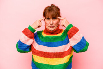 Middle age caucasian woman isolated on pink background focused on a task, keeping forefingers pointing head.