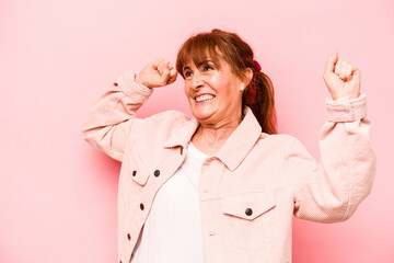 Middle age caucasian woman isolated on pink background celebrating a special day, jumps and raise arms with energy.