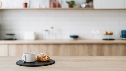 Croissant and coffee on kitchen countertop, against blurred interior