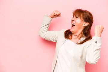 Middle age caucasian woman isolated on pink background raising fist after a victory, winner concept.